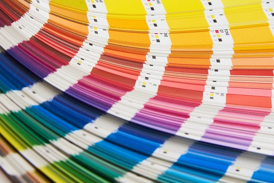 Fanned printed colour swatch guide showing rows of yellow, orange, red, purple, blue, and green colour samples with small square tabs.